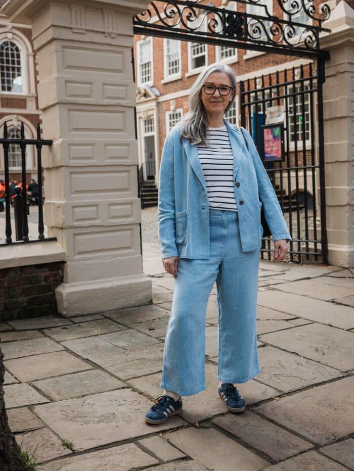 lady wearing light blue linen suit and striped top in front of iron gates